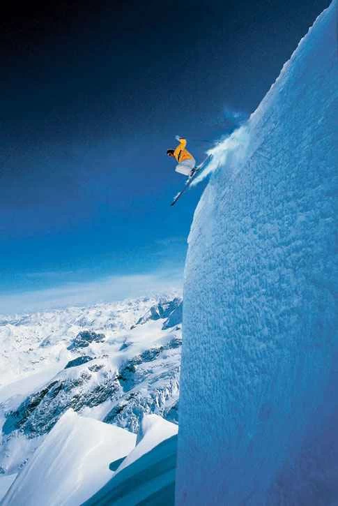 黄色いジャケットを着て雪の崖からスキーをするスキーヤー