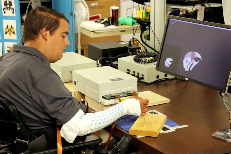 イアン・バークハートは機械を使って右腕を制御し、ペグを持ち上げています。