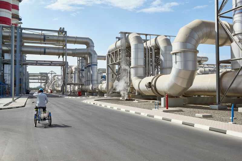 工場を構成する巨大な管の近くで自転車に乗る男性